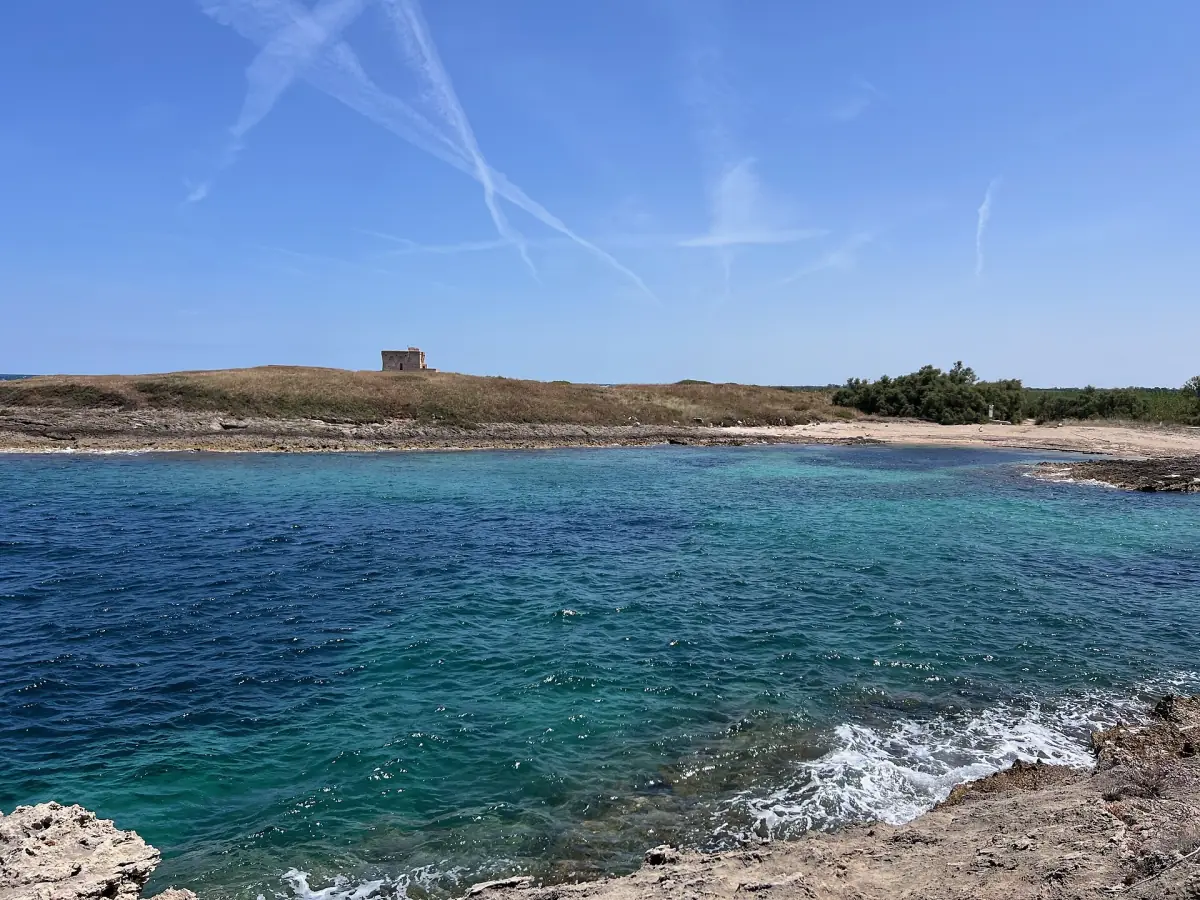 Acqua blu in una baia rocciosa con la torre sullo sfondo